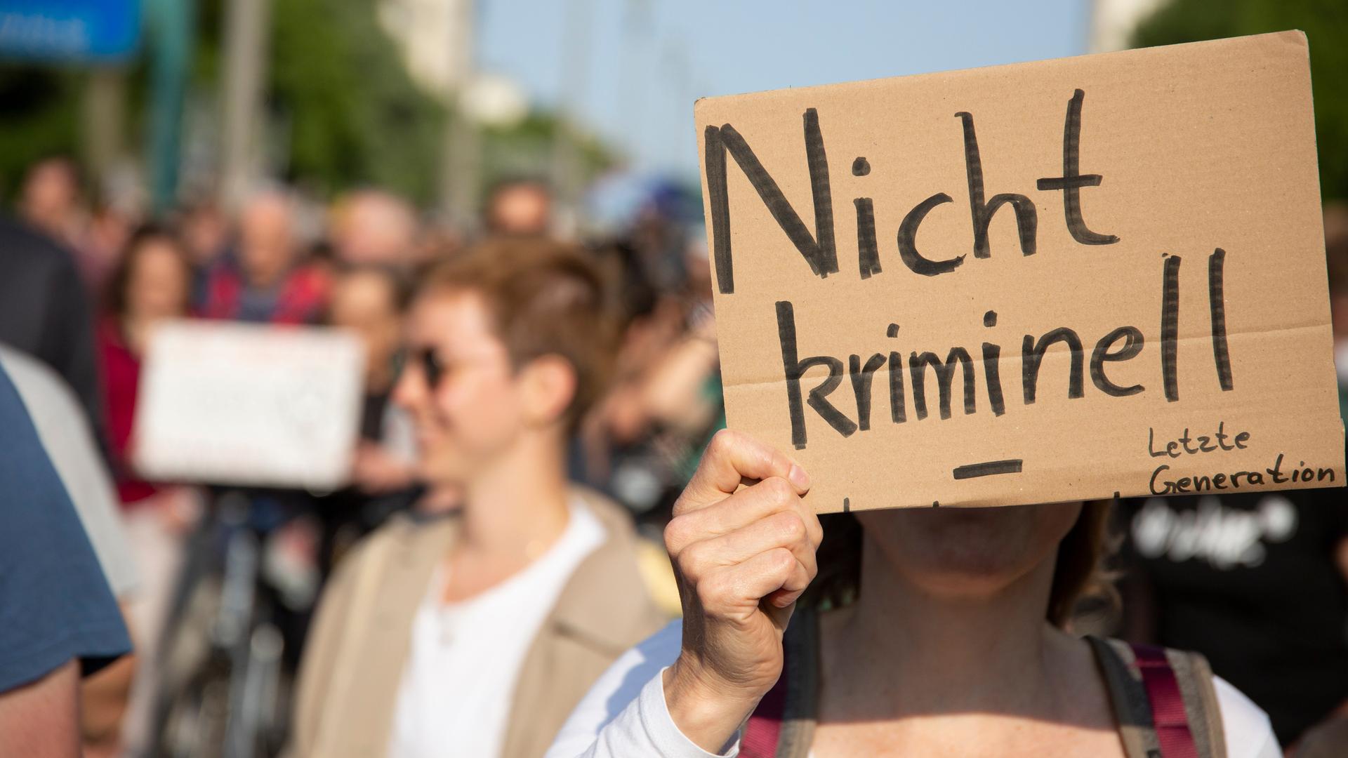 Menschen laufen bei einem Protestmarsch durch die Straßen. Eine Person hält ein Schild vor ihr Gesicht, auf dem "nicht kriminell" steht. Menschen laufen bei einem Protestmarsch durch die Straßen. Eine Person hält ein Schild vor ihr Gesicht, auf dem "nicht kriminell" steht.