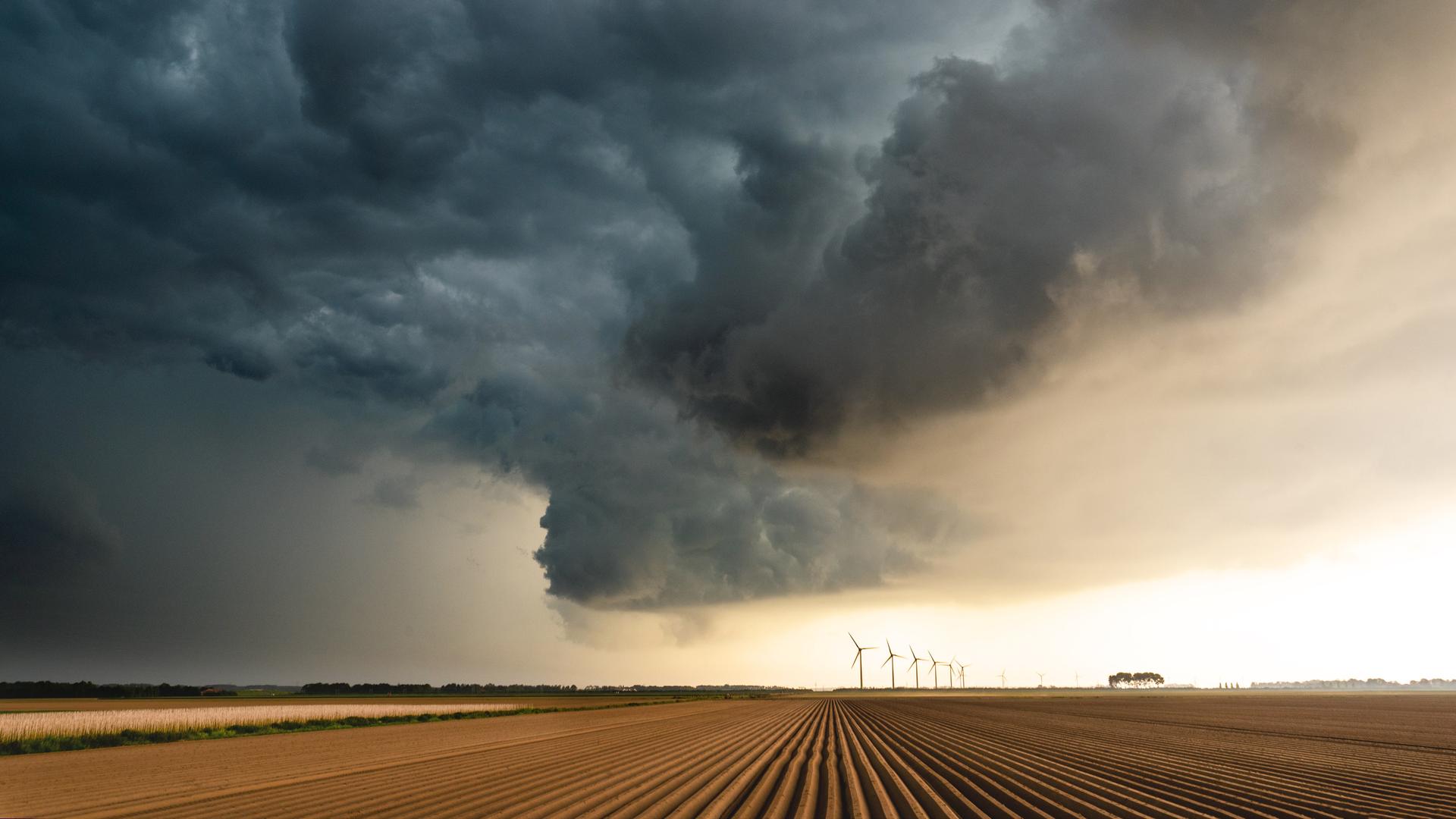 Gewitterwolken über einem Feld. Im Hintergrund sind Windräder zu sehen, während die Sonne langsam durch die Wolken bricht. Gewitterwolken über einem Feld. Im Hintergrund sind Windräder zu sehen, während die Sonne langsam durch die Wolken bricht.