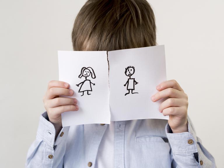 Ein Kind hält sich eine durchgerissene Zeichnung eines Paares vors Gesicht. (Symbolfoto)
