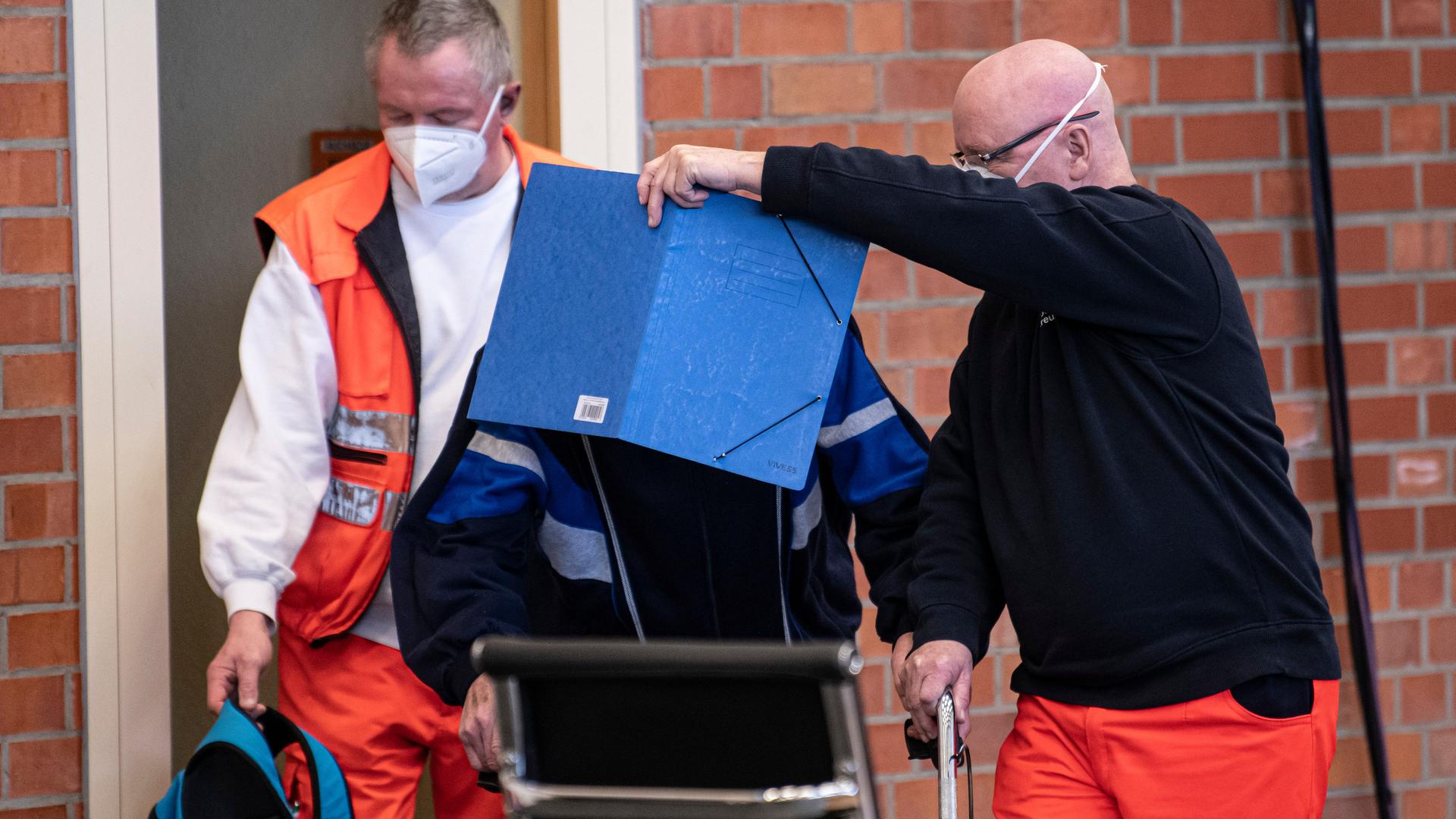 Ein angeklagter ehemaliger KZ-Wachmann kommt mit Hilfe von Sanitätern zur Fortsetzung seines Prozesses in den Gerichtssaal in einer Turnhalle. Ein angeklagter ehemaliger KZ-Wachmann kommt mit Hilfe von Sanitätern zur Fortsetzung seines Prozesses in den Gerichtssaal in einer Turnhalle.
