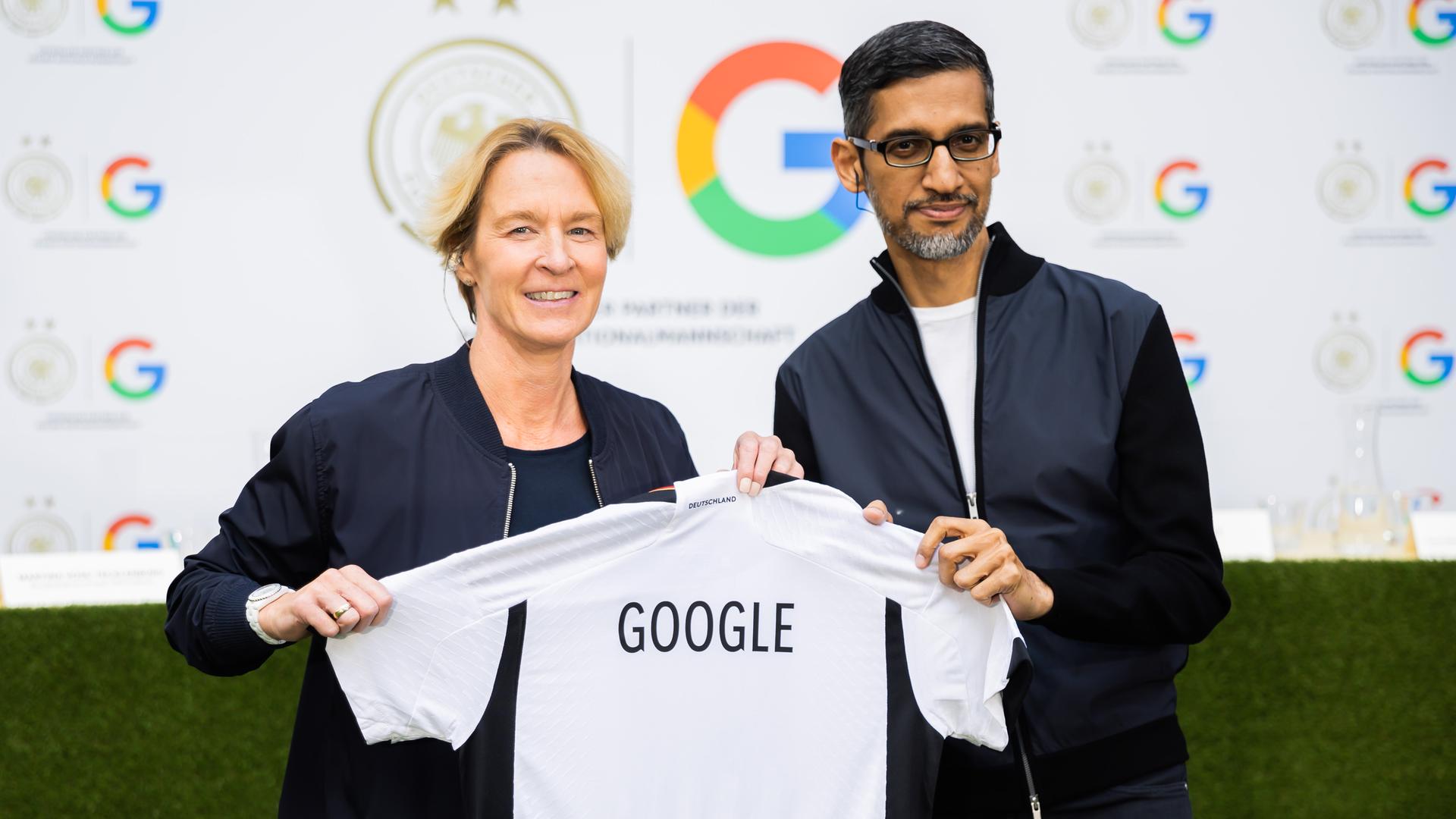 Bundestrainerin Martina Voss-Tecklenburg und Google-Chef Pichai halten gemeinsam ein Shirt mit der Aufschrift "Google" in den Kamera. Bundestrainerin Martina Voss-Tecklenburg und Google-Chef Pichai halten gemeinsam ein Shirt mit der Aufschrift "Google" in den Kamera.