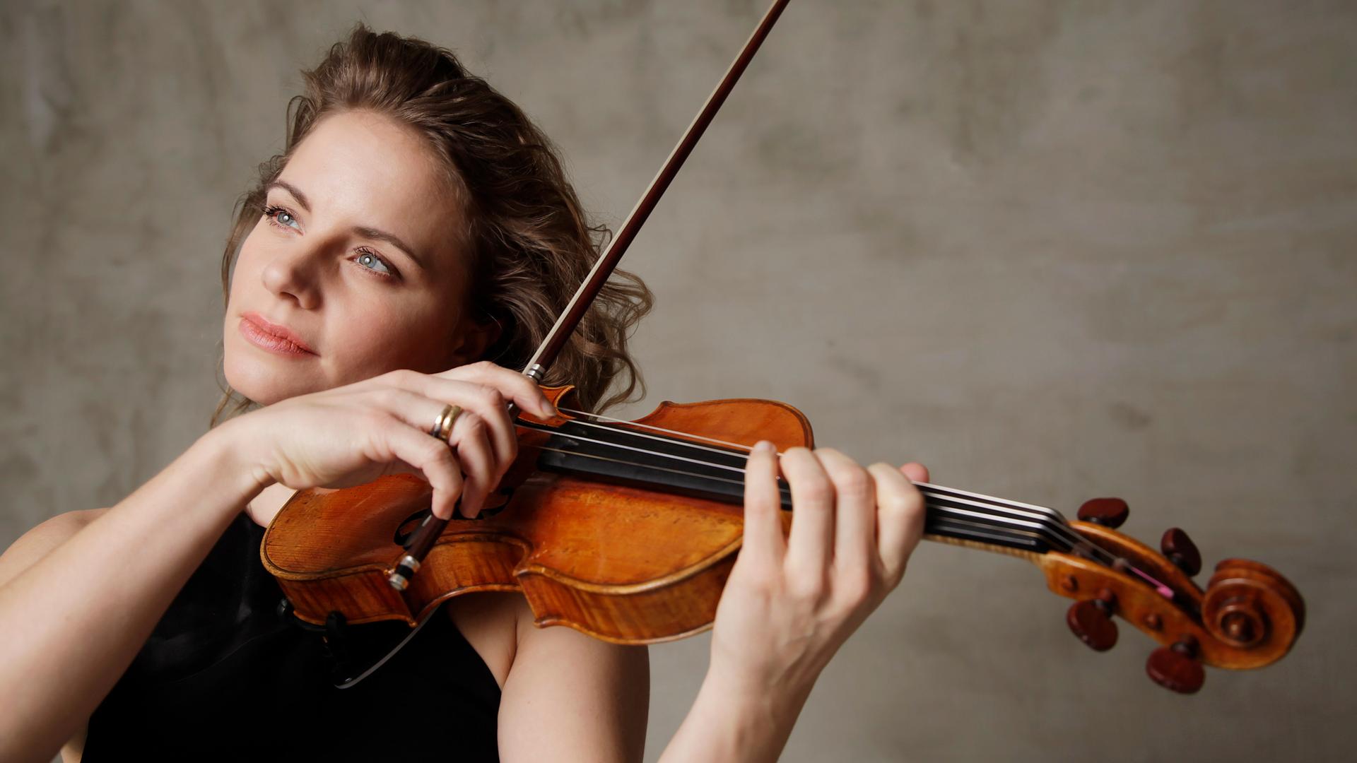 Eine junge Frau, Julia Fischer, spielt mit welligen, offenem Haar und ernstem Blick ihre Geige.