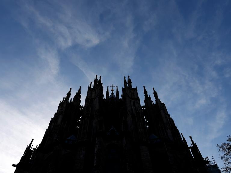 Der Kölner Dom ragt dunkel in einen blauen Himmel hinein.