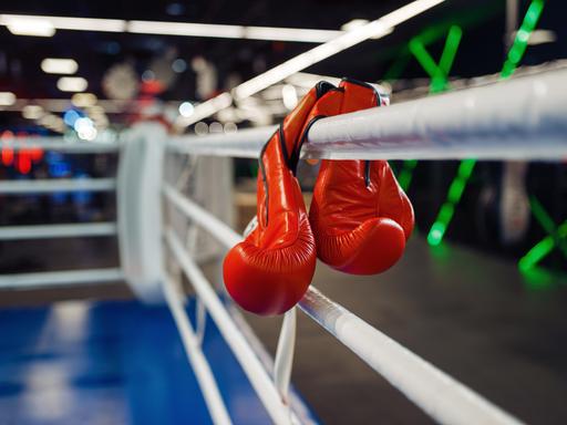 Zwei Boxhandschuhe hängen an einem Boxring.