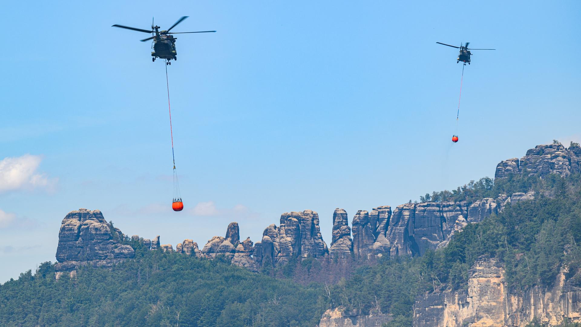 Hubschrauber der Bundeswehr fliegen am 28. Juli mit Löschwasser-Außenlastbehältern um einen Waldbrand im Nationalpark Sächsische Schweiz zu löschen.