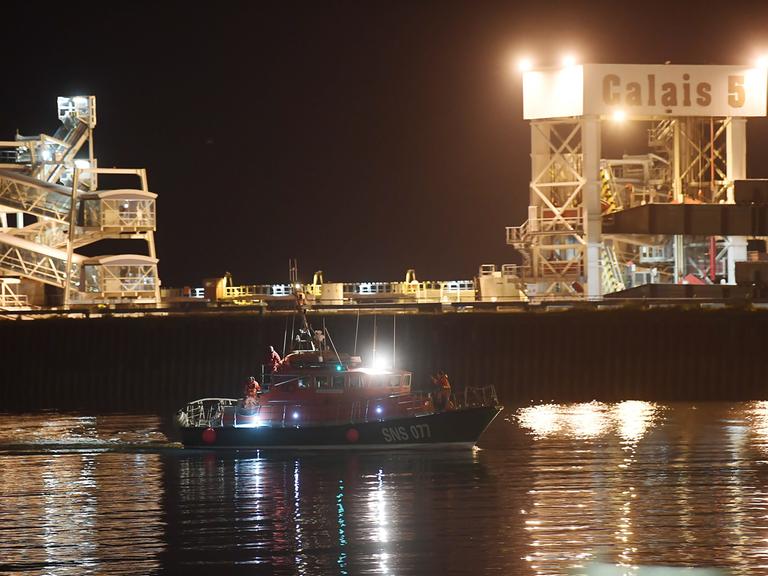 Ein Boot fährt bei Dunkelheit in den Hafen von Calais ein.