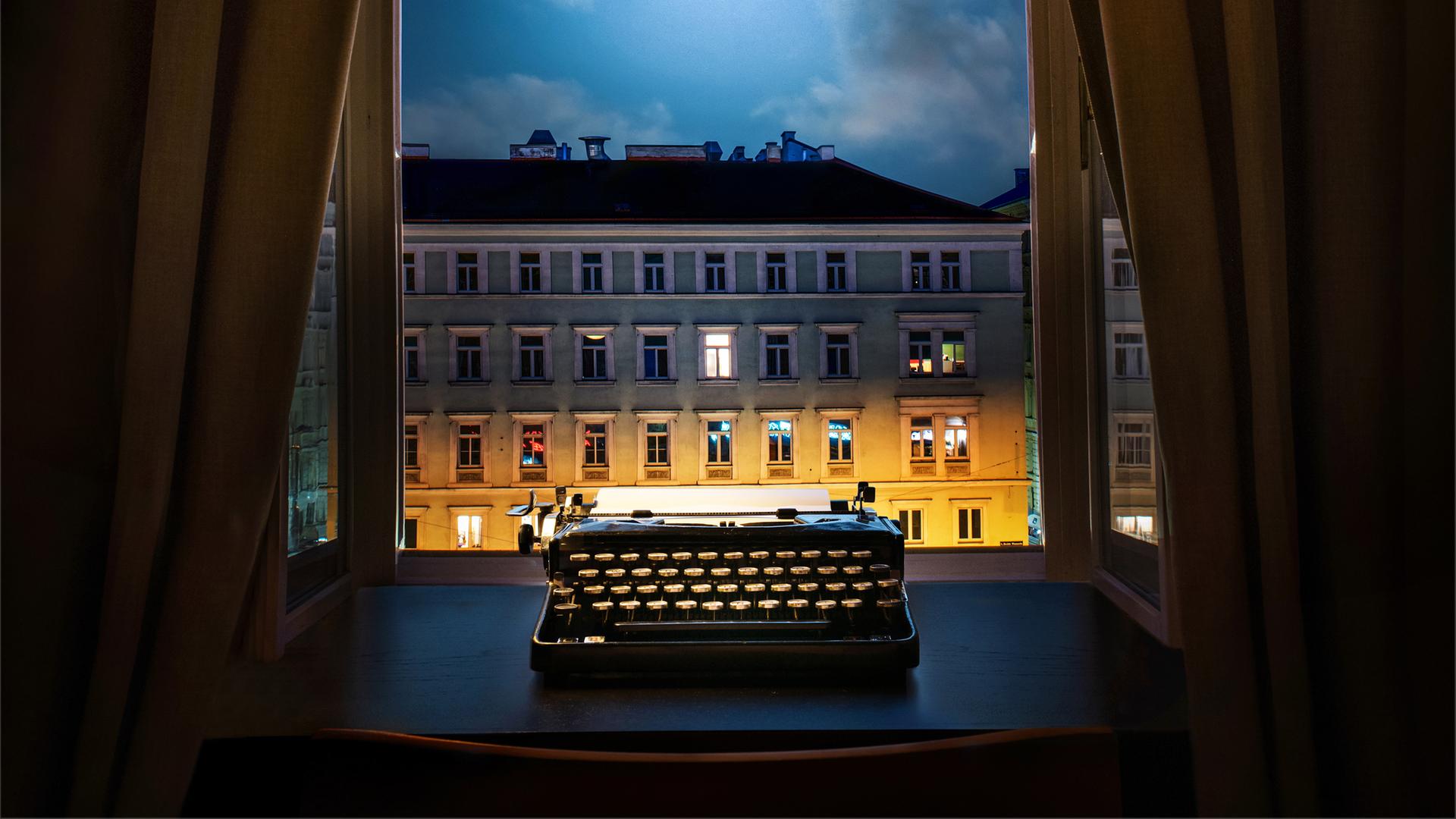 Eine Schreibmaschine steht nachts auf einem Schreibtisch vor dem geöffneten Fenster. Eine Schreibmaschine steht nachts auf einem Schreibtisch vor dem geöffneten Fenster.