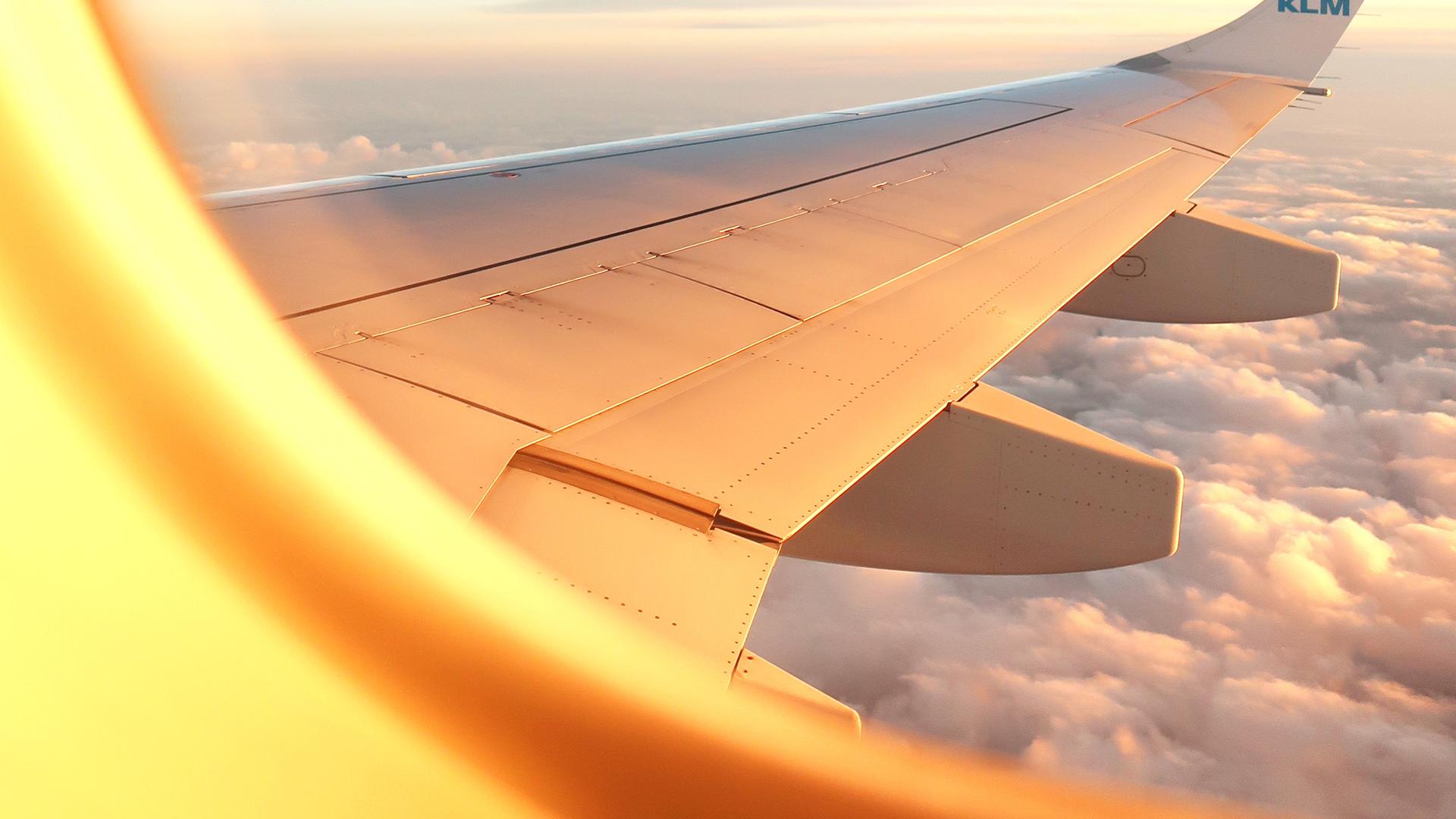 Blick aus dem Kabinenfenster auf die Tragfläche eines Flugzeuges. Im oberen Bereich blauer Himmel, darunter eine dichte, weiße Wolkendecke. Blick aus dem Kabinenfenster auf die Tragfläche eines Flugzeuges. Im oberen Bereich blauer Himmel, darunter eine dichte, weiße Wolkendecke.
