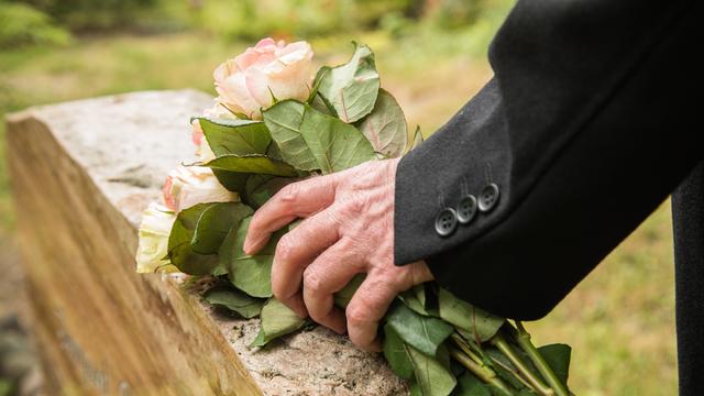 Ein älterer Mann legt in Berlin einen Strauß Rosen auf einen Grabstein (gestellte Szene)
