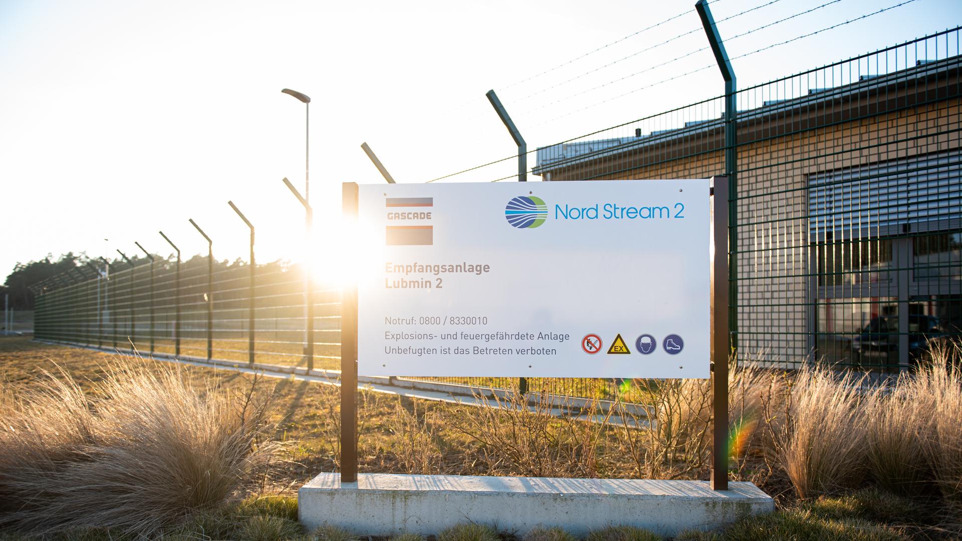 Schild mit der Aufschrift "Nord Stream 2" steht vor einem Zaun und Gebäude. Schild mit der Aufschrift "Nord Stream 2" steht vor einem Zaun und Gebäude.