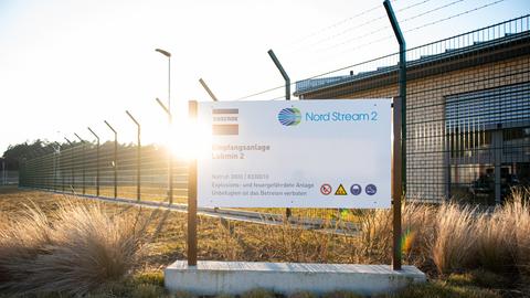 Schild mit der Aufschrift "Nord Stream 2" steht vor einem Zaun und Gebäude.