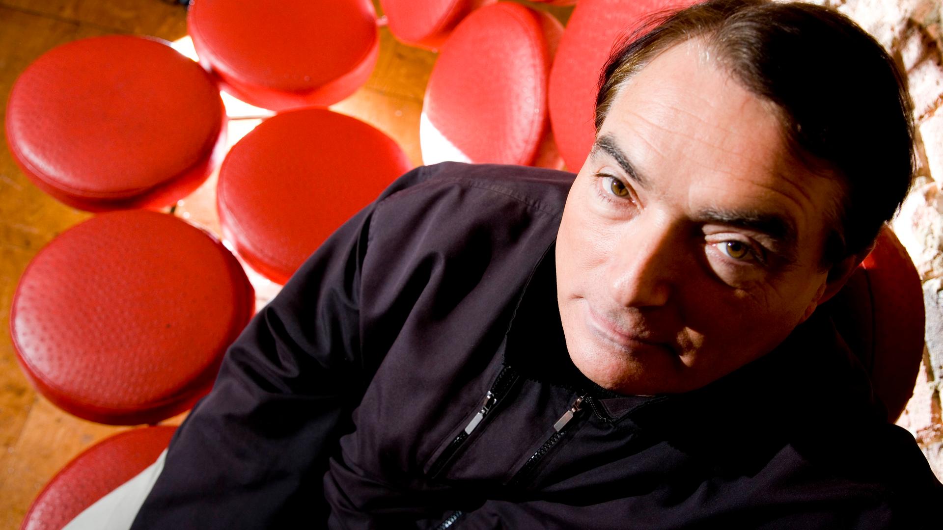 Porträt von Wolfgang Flür, dem Schlagzeuger von Kraftwerk. Er sitzt auf einem "Sofa", dass aus lauter roten Einzelsitzen besteht. Porträt von Wolfgang Flür, dem Schlagzeuger von Kraftwerk. Er sitzt auf einem "Sofa", dass aus lauter roten Einzelsitzen besteht.