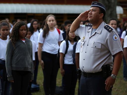 Schülerinnen und Schüler stehen stramm vor einem Offizier in Uniform, der in Richtung Fahne (nicht im Bild) salutiert