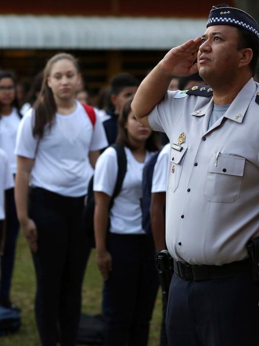 Schülerinnen und Schüler stehen stramm vor einem Offizier in Uniform, der in Richtung Fahne (nicht im Bild) salutiert
