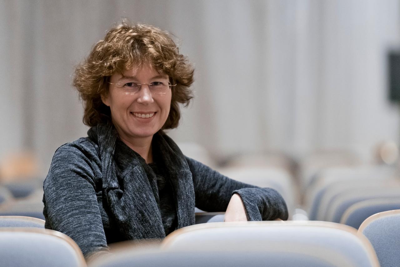 Eine Frau sitzt in einem Hörsaal und schaut feundlich in die Kamera: die Physikerin Sabine Hossenfelder.