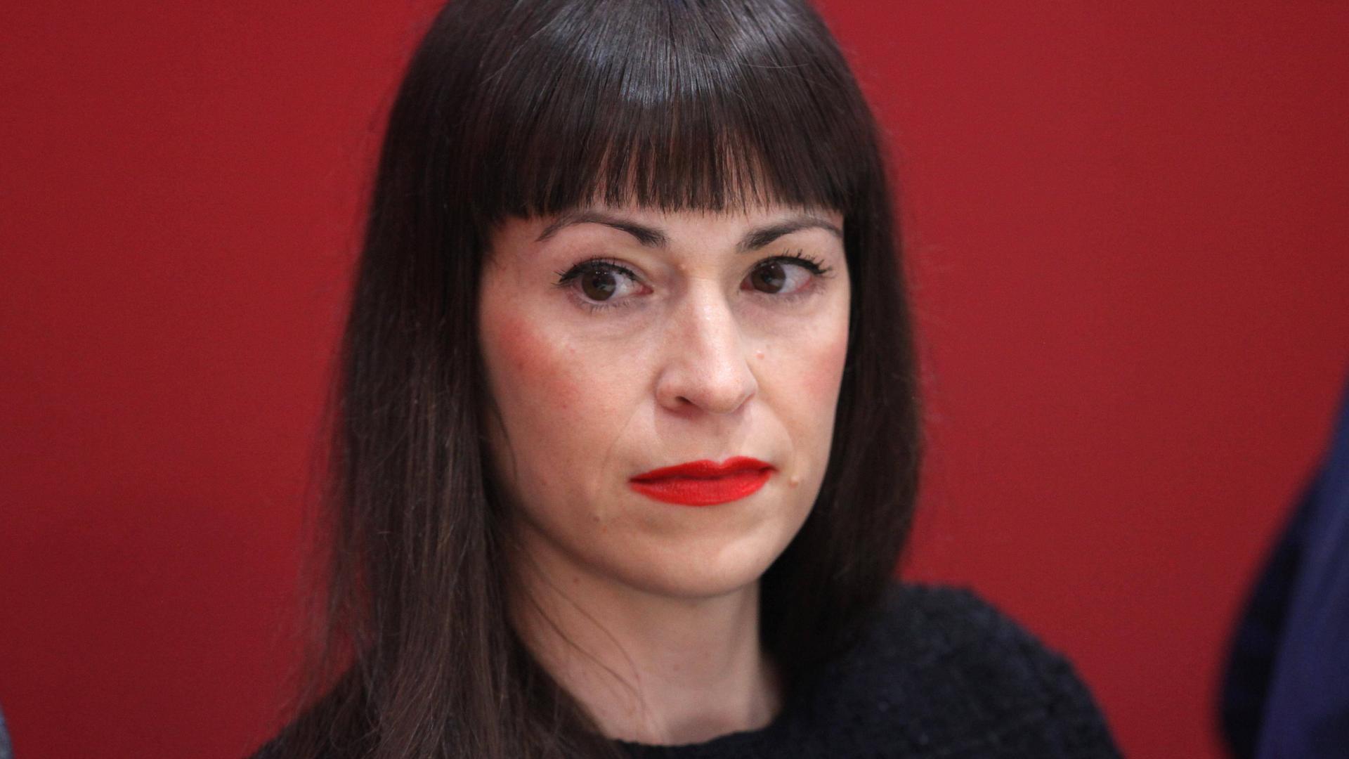 Eine Frau mit schulterlangen braunen Haaren blickt in die Kamera. Hinter ihr ist eine rote Wand. Es ist die Sprachsoziologin Carolin Amlinger. Eine Frau mit schulterlangen braunen Haaren blickt in die Kamera. Hinter ihr ist eine rote Wand. Es ist die Sprachsoziologin Carolin Amlinger.