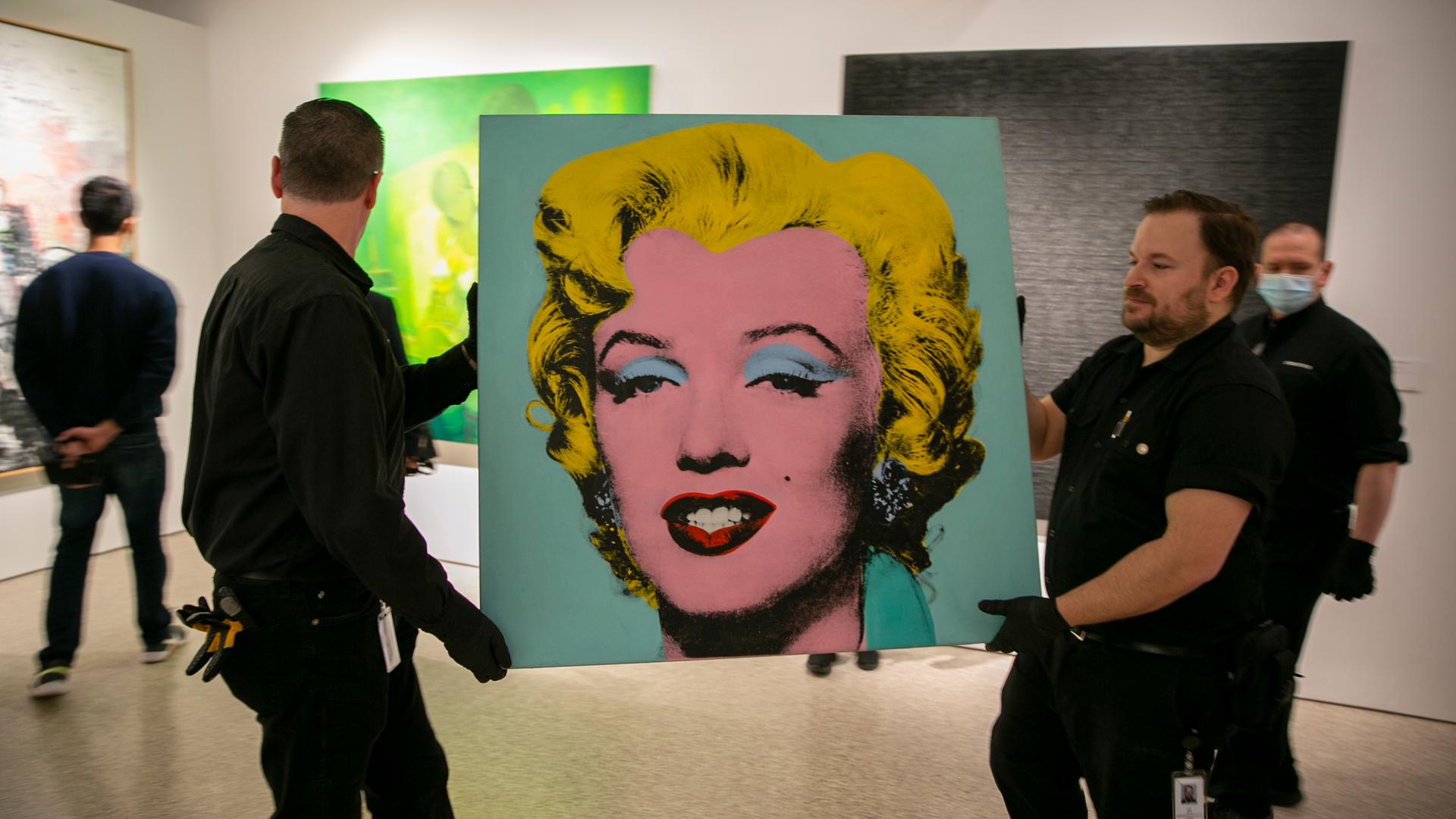 Das Bild "Shot Sage Blue Marilyn" wird von zwei Arbeitern durch eine Galerie getragen.