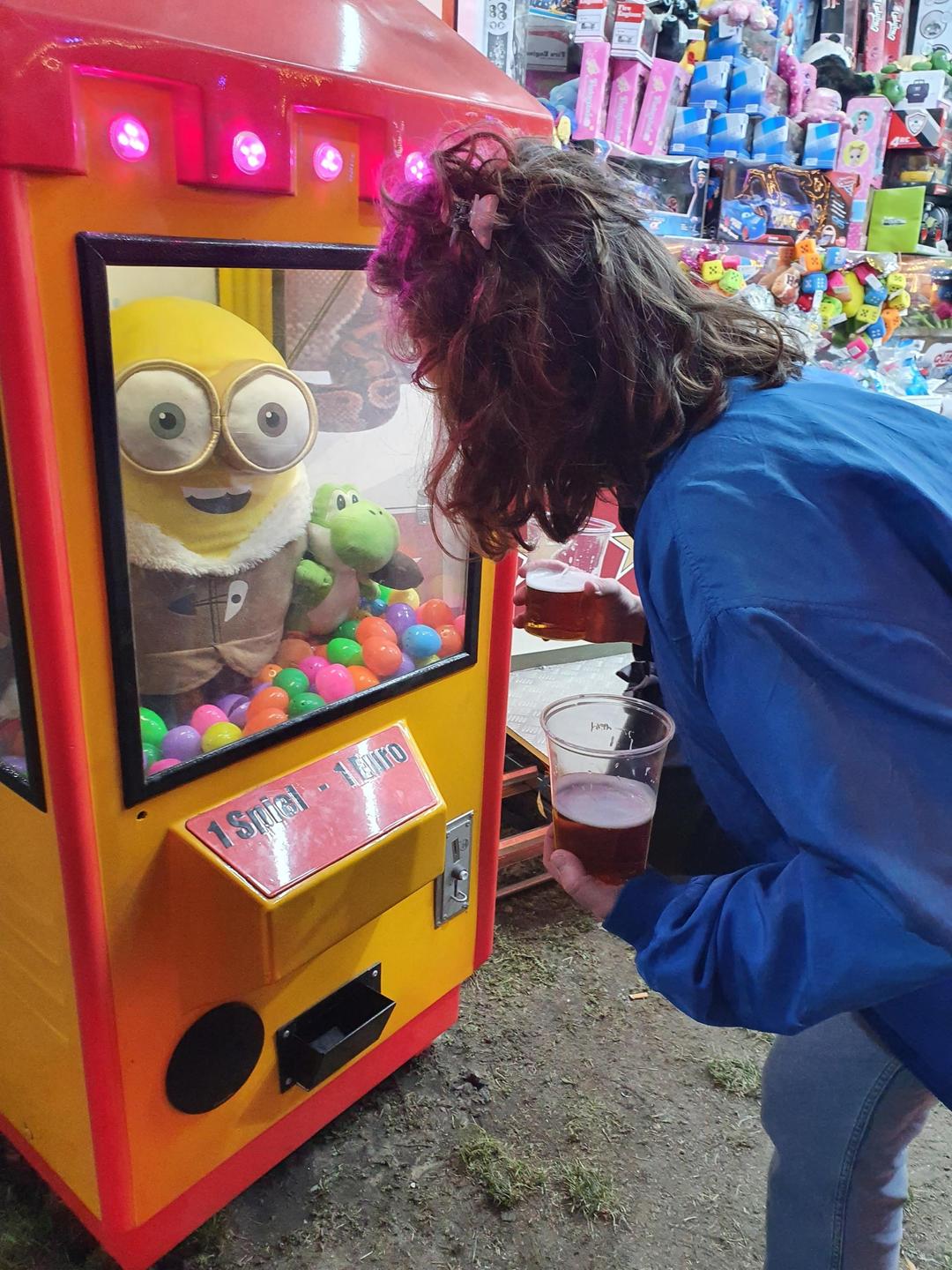 Eine junge Frau beugt sich auf dem Rummelplatz über die Auslage eines Puppen-Automaten und trägt dabei Bier. Eine junge Frau beugt sich auf dem Rummelplatz über die Auslage eines Puppen-Automaten und trägt dabei Bier.