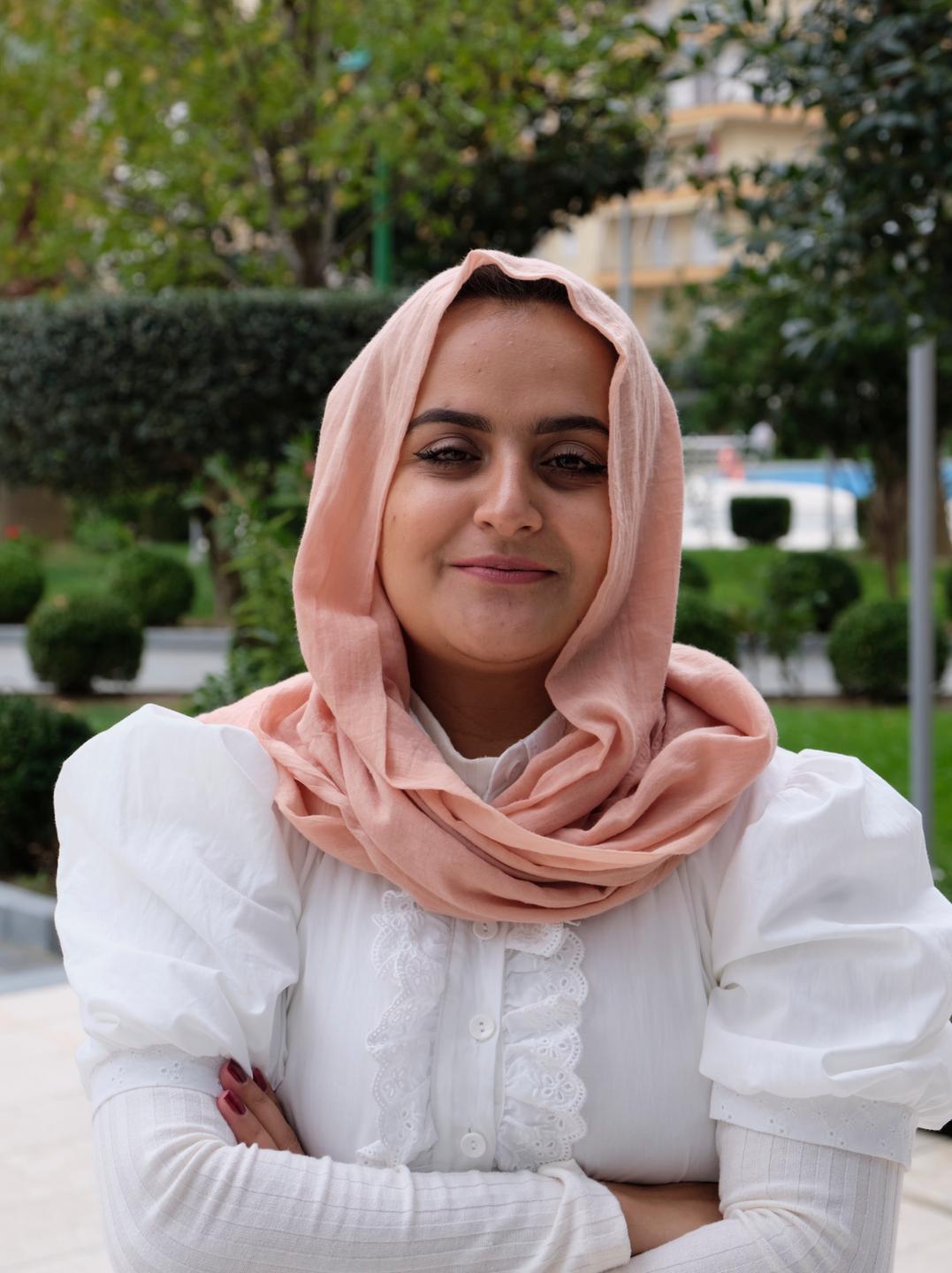 Beheshta Arghand steht in der albanischen Hotelanlage, trägt ein lockeres rosa Kopftuch, eine weiße Bluse und lächelt. Beheshta Arghand steht in der albanischen Hotelanlage, trägt ein lockeres rosa Kopftuch, eine weiße Bluse und lächelt.