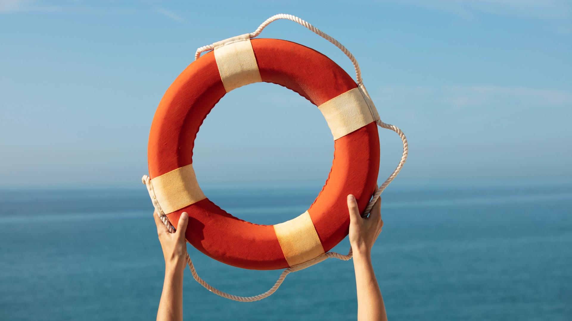 Hände halten einen Rettungsring vor blauem Himmel in die Luft. Hände halten einen Rettungsring vor blauem Himmel in die Luft.