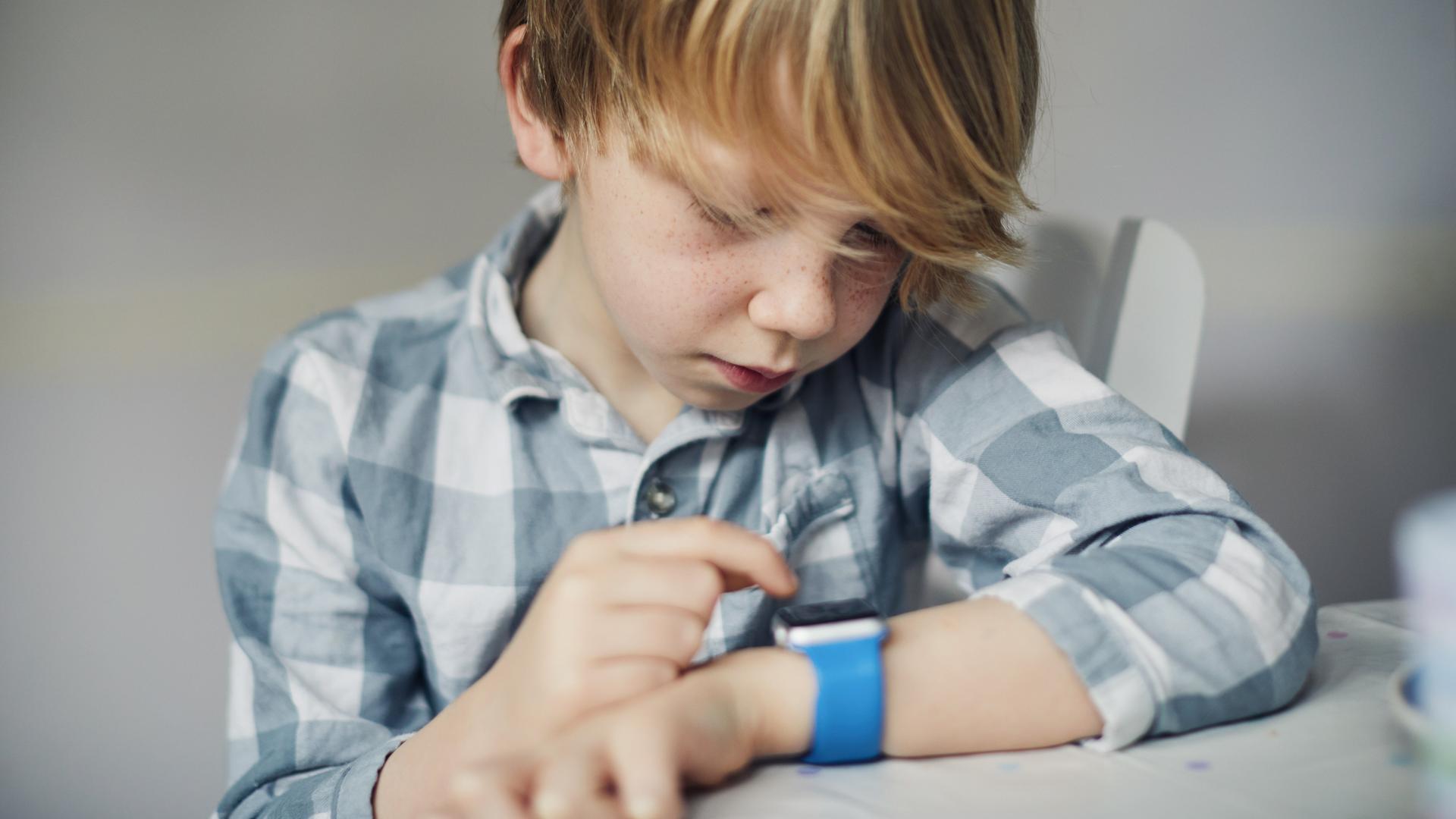 Ein Junge schaut auf sein Handgelenk wo er eine Smartwatch trägt.