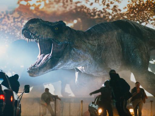 Filmszene aus "Jurassic World 3", ein T-Rex Dinosaurier setzt die Menschen in einem Autokino in Angst und Schrecken.