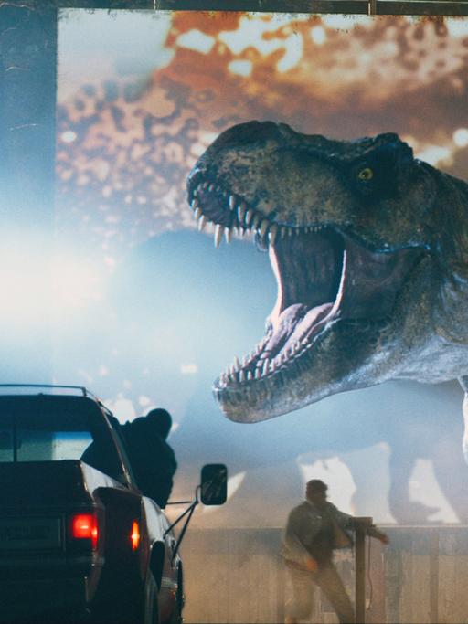 Filmszene aus "Jurassic World 3", ein T-Rex Dinosaurier setzt die Menschen in einem Autokino in Angst und Schrecken.