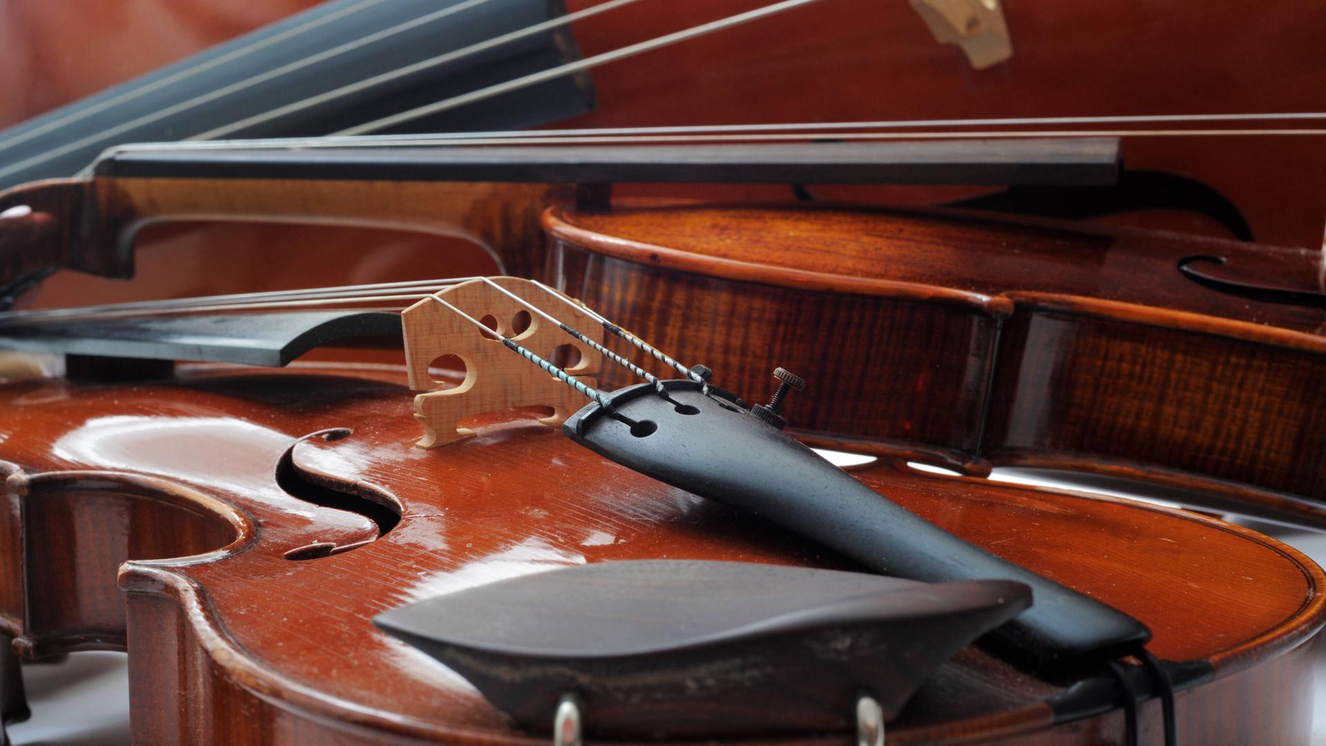Unterschiedliche Streichinstrumente wie Violine, Bratsche und Violoncello liegen nah beieinander. Unterschiedliche Streichinstrumente wie Violine, Bratsche und Violoncello liegen nah beieinander.