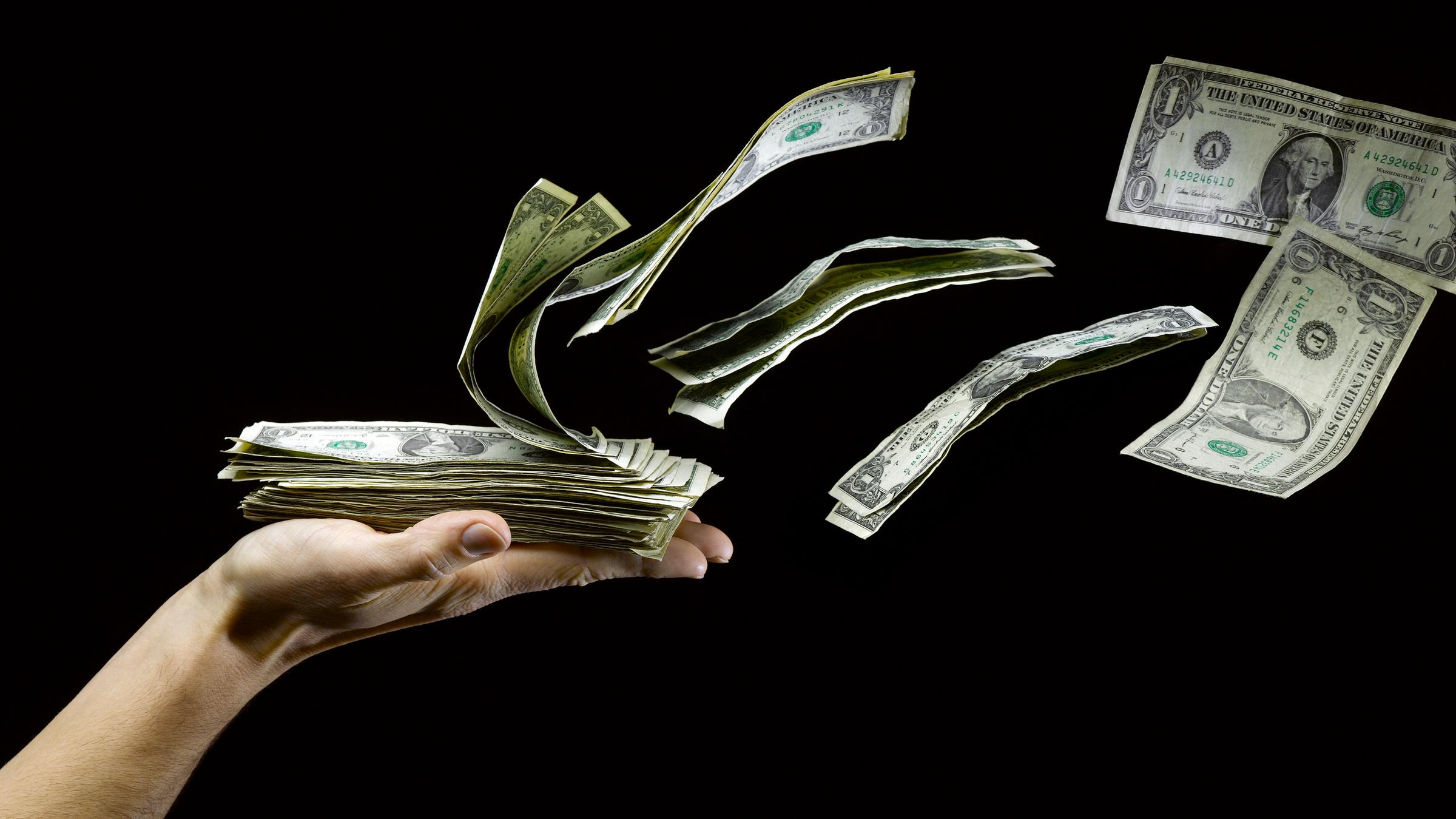 US Dollar fliegen von einer ausgestreckten Hand, die einen Haufen Geldscheine hält. US Dollar fliegen von einer ausgestreckten Hand, die einen Haufen Geldscheine hält.