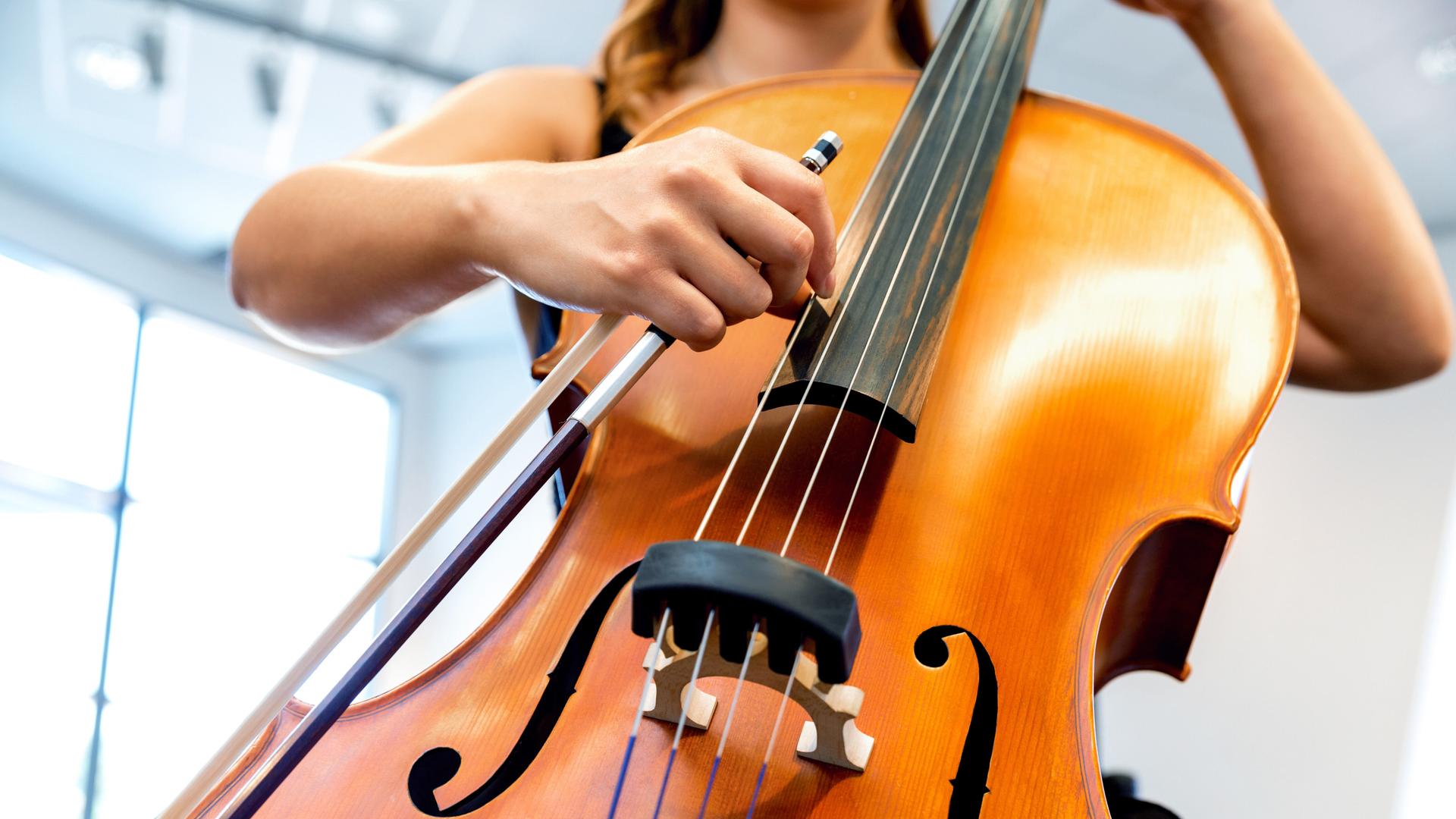 Blick auf die Hände einer jungen Frau, die ein Violoncello spielt. 