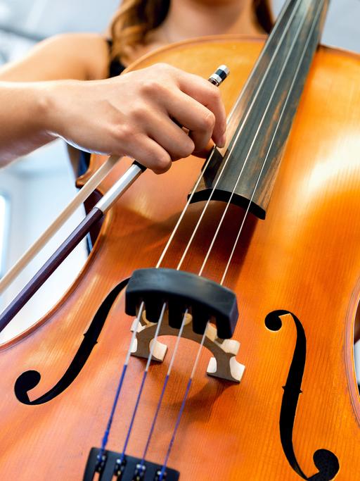 Blick auf die Hände einer jungen Frau, die ein Violoncello spielt. 