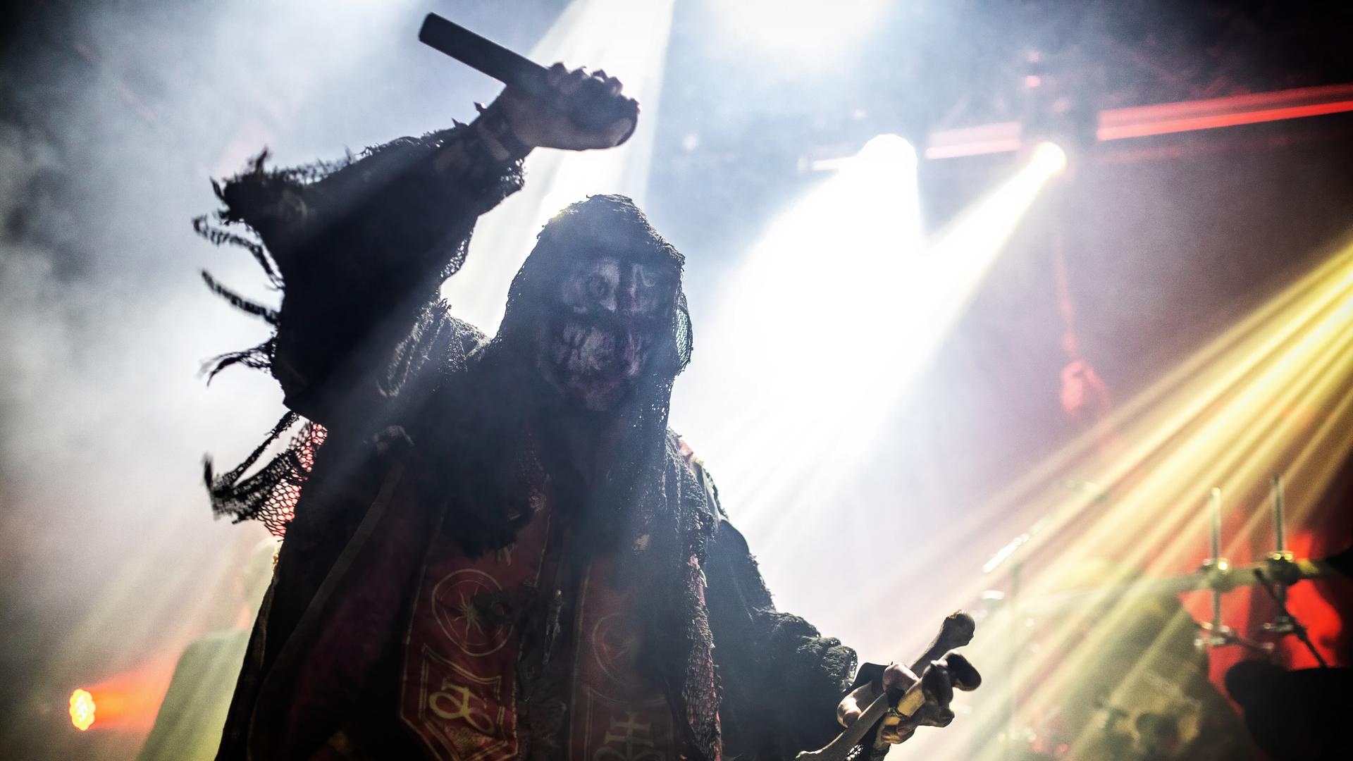 Der Sänger der norwegischen Black-Metal-Band Mayhem, Attila Csihar, in Kostüm und mit erhobenem Arm bei einem Konzert in der Rockefeller Music Hall in Oslo im Jahr 2022.
