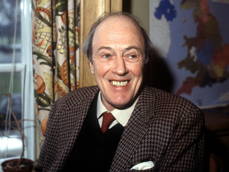 Roald Dahl trägt ein kariertes Jacket und lacht in die Kamera.