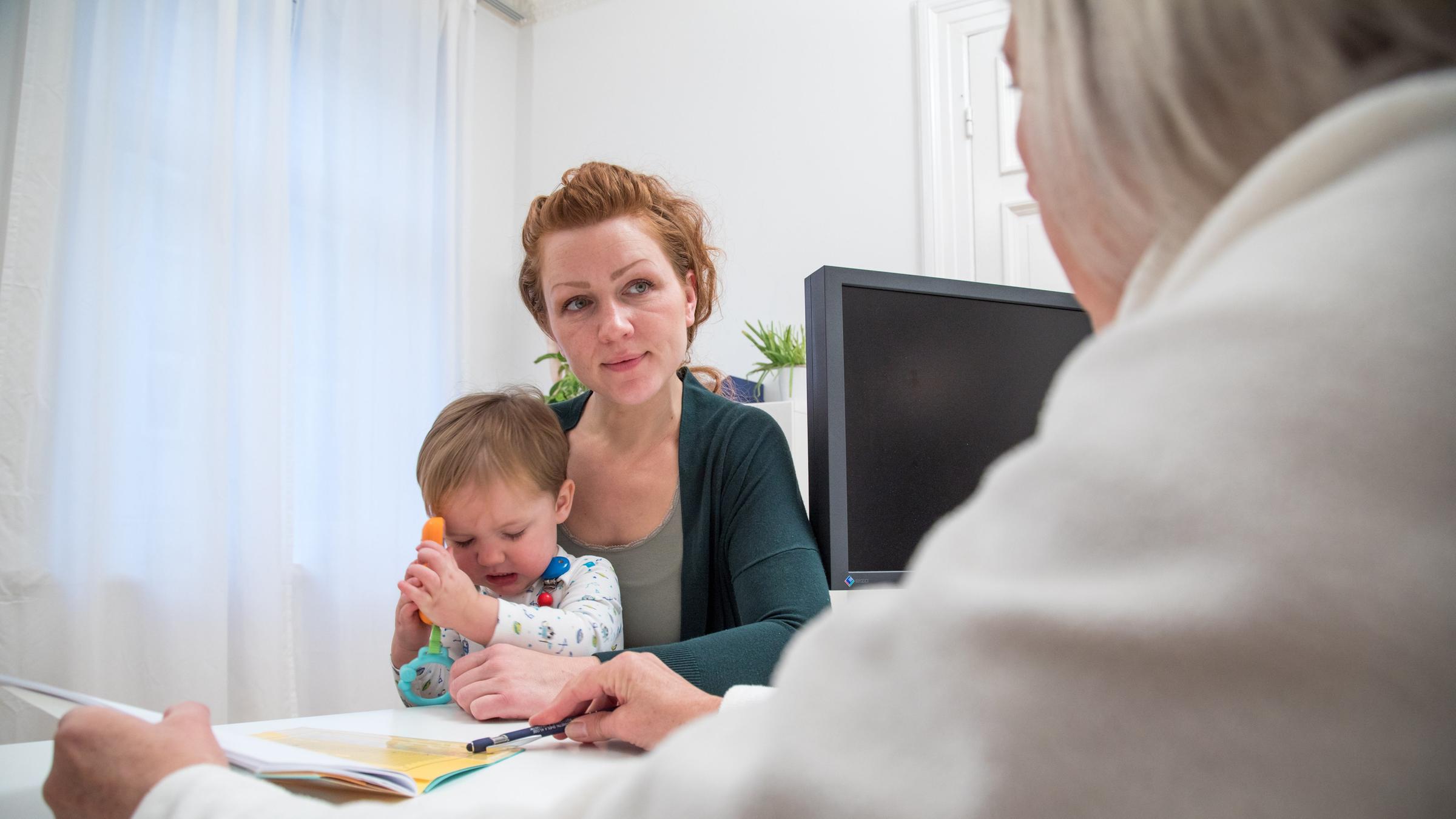 Symbolbild: Mutter mit Kind mit Ärztin im Sprechzimmer