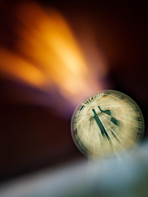 Eine Bitcoin Münzeverschwimmt vor einer Flamme.