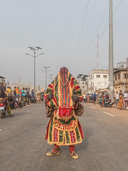 Ein Egoun steht auf einer Straße in Porto Novo: Ein Mann, in bunte weite Stoffe gewandet, die auch das Gesicht verhüllen.