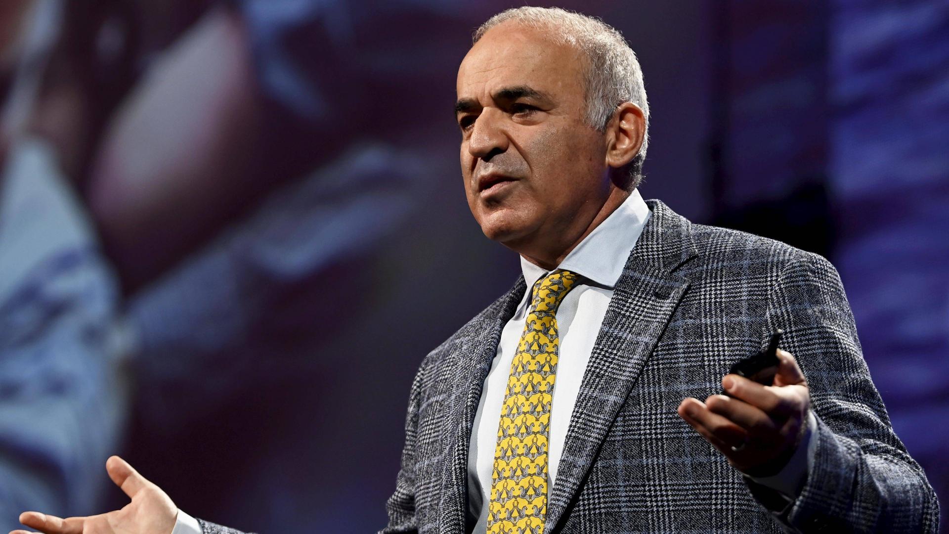 Garri Kasparow steht auf einer Bühne mit ausgebreiteten Händen