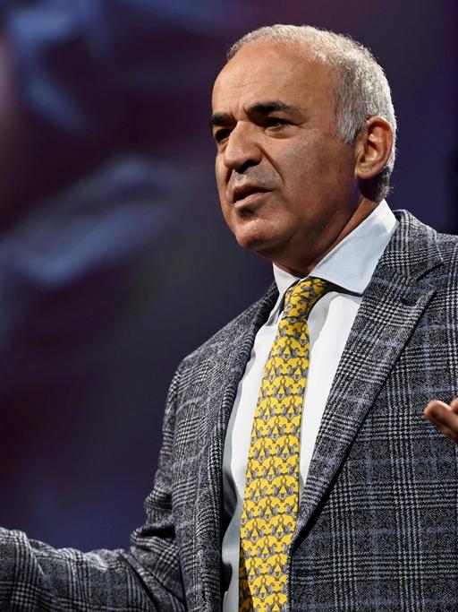 Garri Kasparow steht auf einer Bühne mit ausgebreiteten Händen