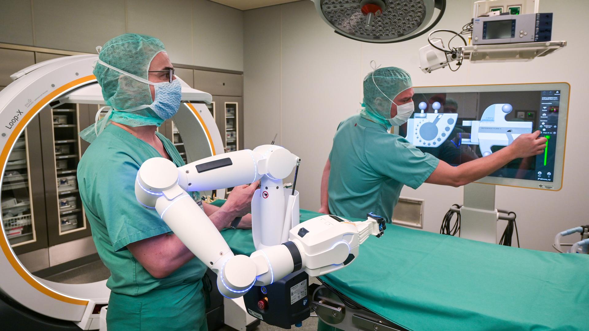 Zwei Ärzte verfolgen auf dem Bildschirm die OP, welche durch einen Roboter unterstützt wird. Zwei Ärzte verfolgen auf dem Bildschirm die OP, welche durch einen Roboter unterstützt wird.