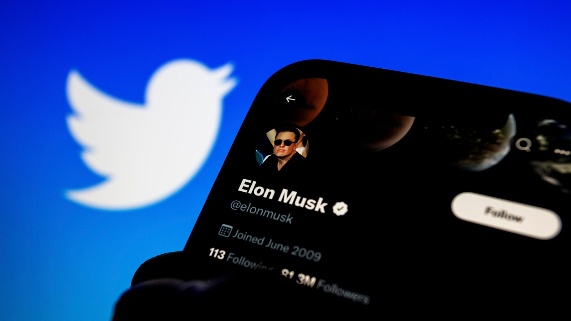Ein Smartphone mit dem Bild von Elon Musk auf dem Bildschirm, im Hintergrund das Logo der Plattform "Twitter".