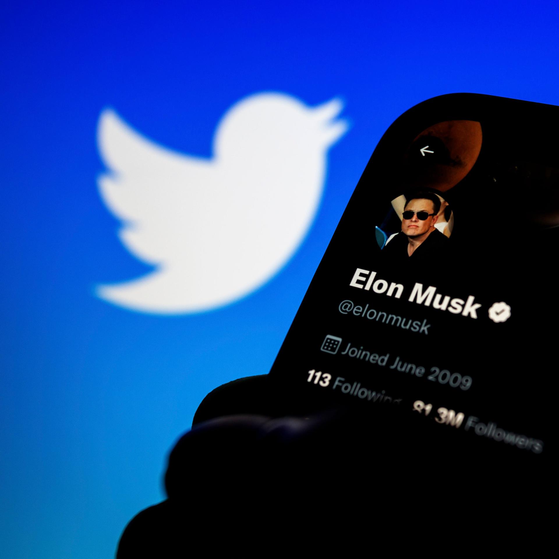 Symbolbild: Ein Smartphone mit dem Bild von Elon Musk auf dem Bildschirm, im Hintergrund das Logo der Plattform "Twitter".