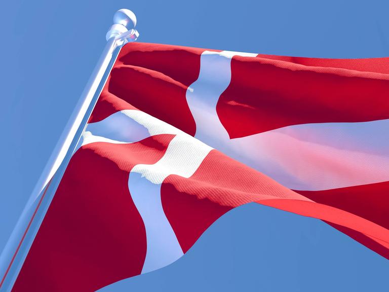 Eine dänische Flagge weht im Wind unter blauem Himmel.