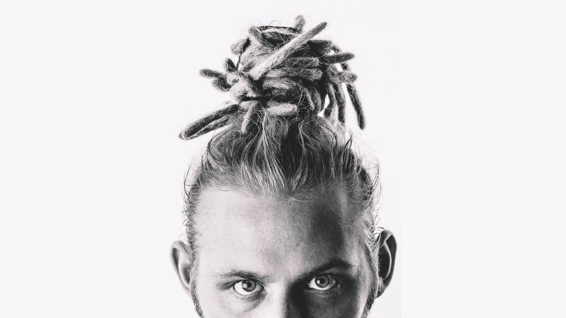 Foto eines weißen Mannes mit Dreadlocks. Er trägt sie als Dutt auf dem Kopf. Das Foto ist schwarzweiß und unter seinen Augen abgeschnitten. Foto eines weißen Mannes mit Dreadlocks. Er trägt sie als Dutt auf dem Kopf. Das Foto ist schwarzweiß und unter seinen Augen abgeschnitten.