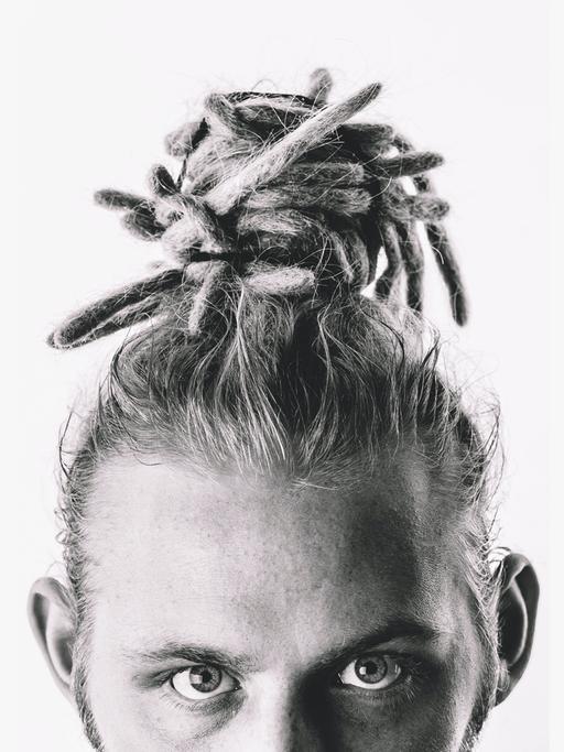 Foto eines weißen Mannes mit Dreadlocks. Er trägt sie als Dutt auf dem Kopf. Das Foto ist schwarzweiß und unter seinen Augen abgeschnitten. 