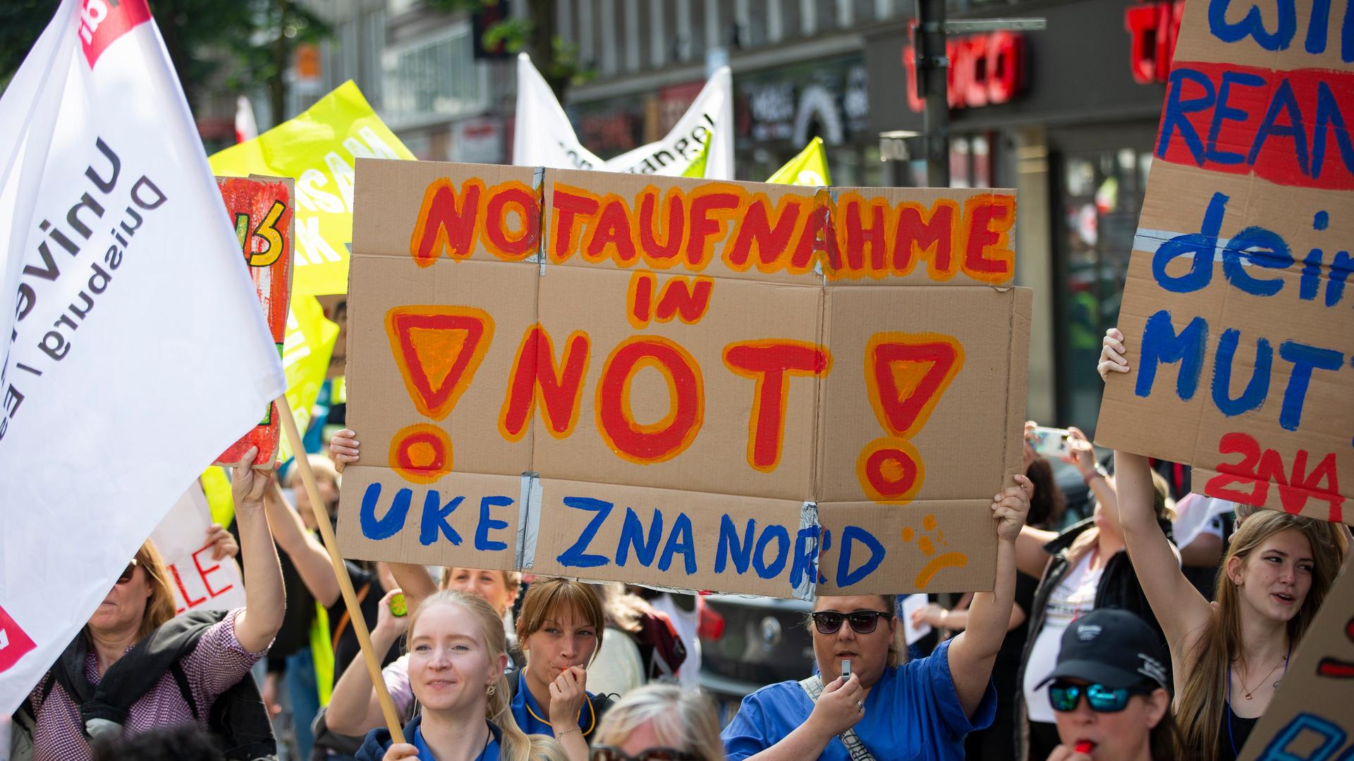 Demonstrantinnen tragen ein Schild mit der Aufschrift "Notaufnahme in Not! UKE ZNA Nord". Zahlreiche Demonstranten aus dem Gesundheitsbereich ziehen durch die Düsseldorfer Innenstadt in Richtung Nordrhein-Westfälischer Landtag. Die Gewerkschaft Verdi hatte zur Demonstration für Unikliniken unter dem Motto "Wir für Euch, ihr für uns" aufgerufen. Demonstrantinnen tragen ein Schild mit der Aufschrift "Notaufnahme in Not! UKE ZNA Nord". Zahlreiche Demonstranten aus dem Gesundheitsbereich ziehen durch die Düsseldorfer Innenstadt in Richtung Nordrhein-Westfälischer Landtag. Die Gewerkschaft Verdi hatte zur Demonstration für Unikliniken unter dem Motto "Wir für Euch, ihr für uns" aufgerufen.