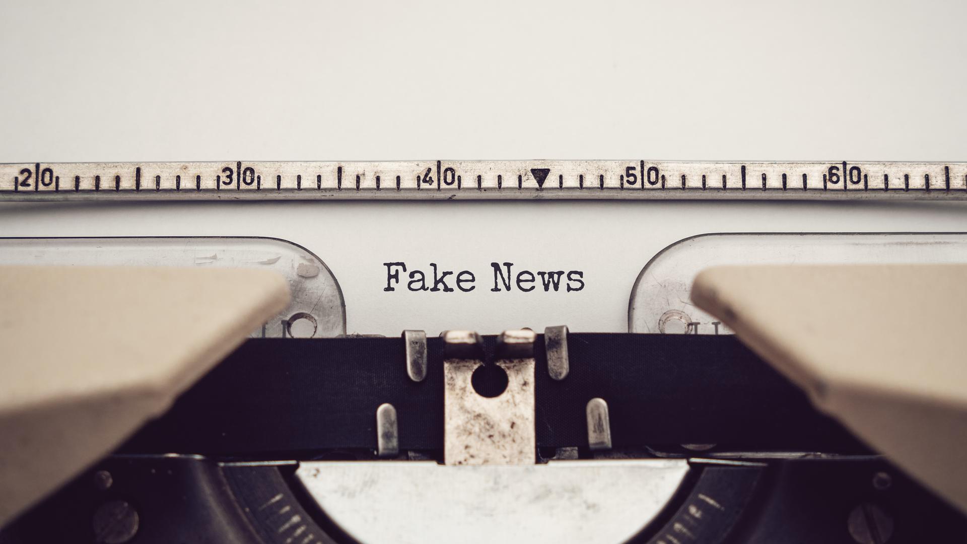 Nahaufnahme einer analagen Schreibmaschine, mit der die Wörter "Fake News" auf ein eingespanntes Blatt Papier getippt wurden. Nahaufnahme einer analagen Schreibmaschine, mit der die Wörter "Fake News" auf ein eingespanntes Blatt Papier getippt wurden.