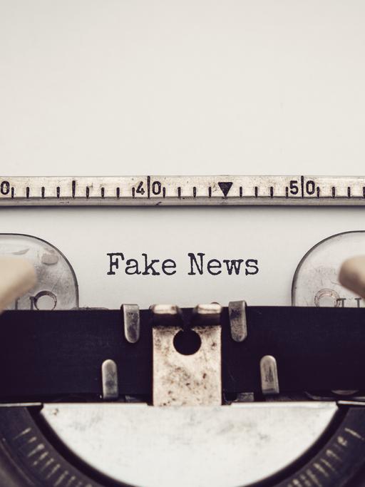 Nahaufnahme einer analagen Schreibmaschine, mit der die Wörter "Fake News" auf ein eingespanntes Blatt Papier getippt wurden.
