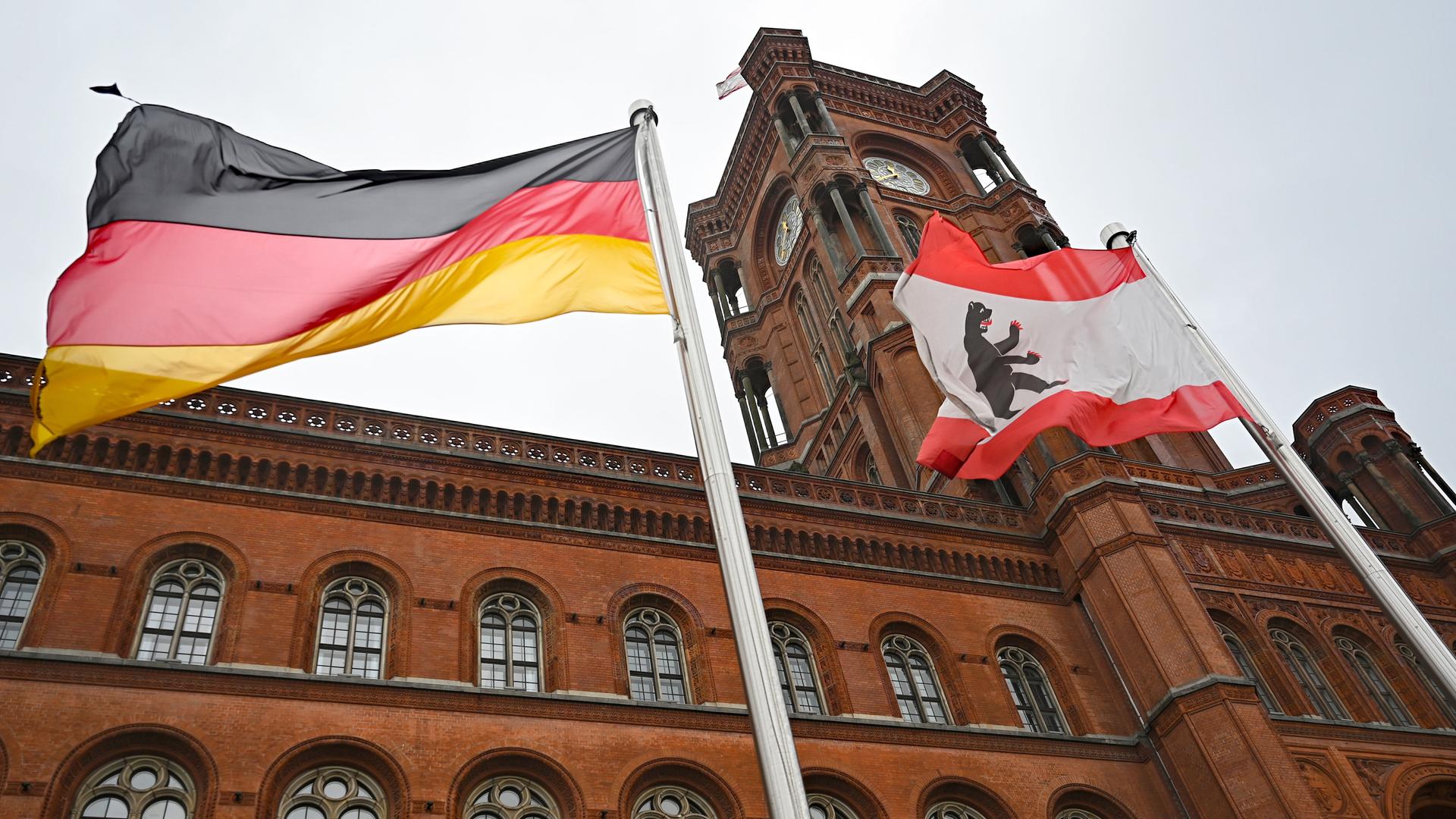 Das Rote Rathaus von Berlin von außen. Im Vordergrund weht eine Deutschland- und eine Berlin-Flagge.