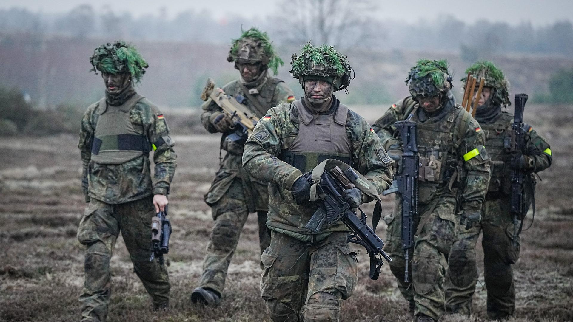 Bundeswehrsoldaten nehmen an einer Übung im Beisein des Verteidigungsministers bei dessen Antrittsbesuch bei der Bundeswehr auf dem Truppenübungsplatz Altengrabow teil. Fünf Soldaten mit Bewaffnung und Kampfmontur gehen durchs Gelände. Bundeswehrsoldaten nehmen an einer Übung im Beisein des Verteidigungsministers bei dessen Antrittsbesuch bei der Bundeswehr auf dem Truppenübungsplatz Altengrabow teil. Fünf Soldaten mit Bewaffnung und Kampfmontur gehen durchs Gelände.