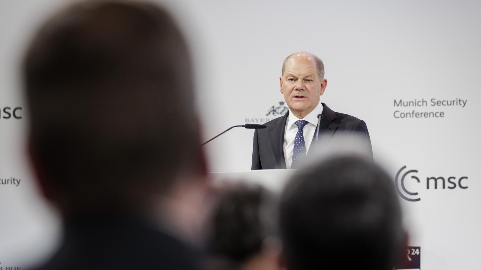 Olaf Scholz (SPD), deutscher Bundeskanzler, steht im Rahmen der Eröffnungsveranstaltung der 59. Münchner Sicherheitskonferenz am 17.02.2023 hinter einem Rednerpult. Im Vordergrund sind Köpfe von hinten zu sehen. 
